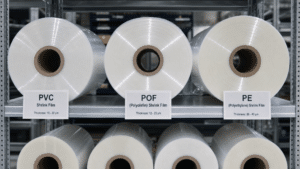 Tipos de Filmes Termoencolhíveis: PVC, POF e PE Rolos de filmes termoencolhíveis PVC, POF e PE organizados em prateleiras industriais com etiquetas identificando cada tipo